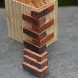 Puede incluir: Primer plano de una pared de ladrillo hecha de pequeños ladrillos rojos y negros. Los ladrillos están dispuestos en un patrón escalonado, creando un efecto de pared de ladrillo realista.