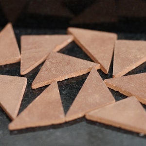 May include: A set of ten terracotta triangle tiles arranged in a starburst pattern on a black surface.