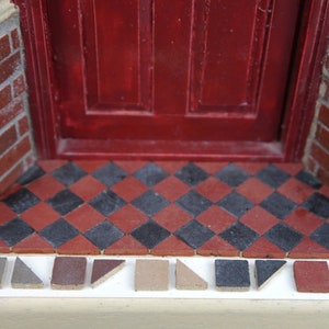 Puede incluir: Primer plano de una puerta roja con un suelo de baldosas de ajedrez negro y rojo. Una fila de pequeñas baldosas de varios colores y formas se coloca sobre una superficie blanca delante de la puerta.