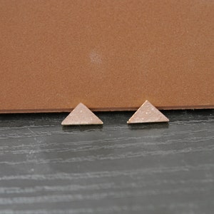 May include: Two small triangle-shaped earrings made of brown speckled clay.