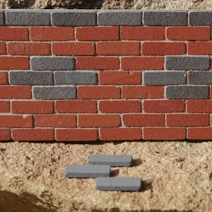 May include: A brick wall with a pattern of red and gray bricks. There are four gray bricks in the foreground.