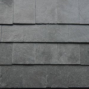 Puede incluir: Primer plano de un tejado de pizarra gris oscuro. Las tejas están dispuestas en forma de espiga, creando una superficie texturizada.