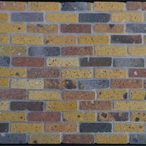 May include: A brick wall with a mix of yellow, brown, and gray bricks. The bricks have a rough texture and are arranged in a staggered pattern.