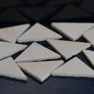 May include: A collection of beige triangular ceramic tiles arranged in a random pattern on a black surface.