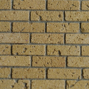 May include: A close-up of a brick wall with a light brown color. The bricks are arranged in a staggered pattern, creating a textured surface.