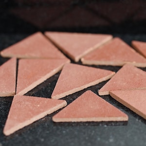 May include: A collection of ten terracotta triangle tiles arranged in a random pattern on a black surface.