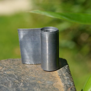 May include: A roll of grey lead sheet, a material used for roofing and flashing, is sitting on a grey rock.