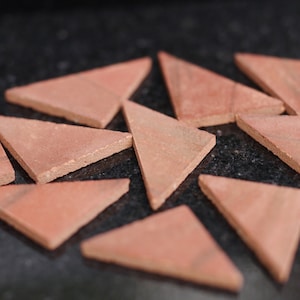 May include: A collection of terracotta triangle tiles in various sizes and shades of red, arranged on a black surface.