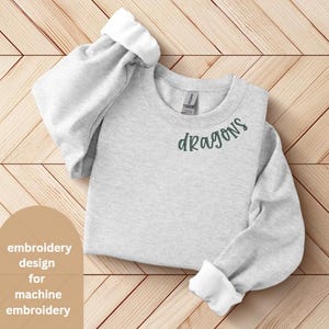 May include: Gray sweatshirt with the word "dragons" embroidered in green on the front. The sweatshirt is folded and laid out on a wooden surface.