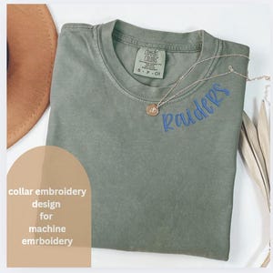 May include: A green t-shirt with a blue embroidered "Raiders" design on the collar. The shirt is made by Comfort Colors and has a tag on the collar.