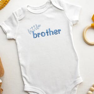 May include: White baby onesie with blue text that reads "little brother".