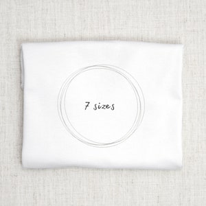 May include: White t-shirt with a circle design and the text "7 sizes" in black.