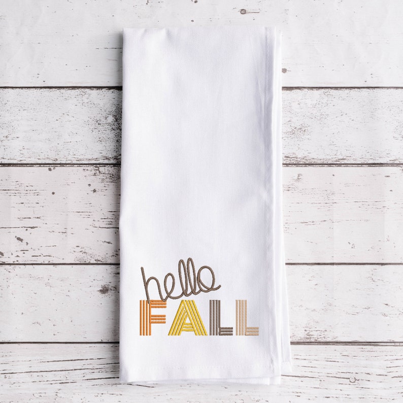 Puede incluir: Toalla de cocina blanca con el texto "hello fall" bordado en marr&oacute;n, amarillo y naranja.