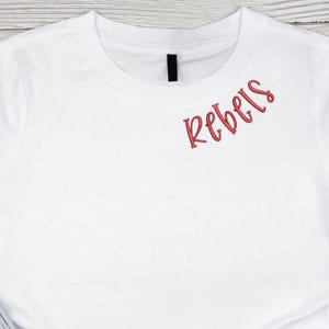 May include: White t-shirt with the word "Rebels" embroidered in red on the right shoulder.