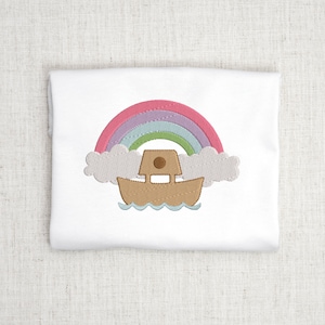 May include: Embroidered design of a rainbow with a brown boat sailing under it. The rainbow is made of pink, purple, blue, and green. The boat has a brown roof and a small window.