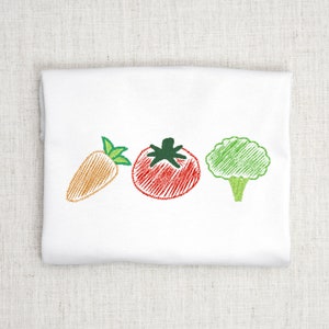 以下が含まれることがあります： 白い布地に刺繍されたニンジン、トマト、ブロッコリーのデザイン