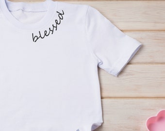 May include: White t-shirt with the word "blessed" written in black cursive across the neckline.