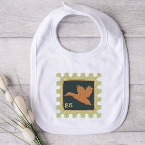 May include: White baby bib with a green and orange embroidered stamp design featuring a flying duck and the text "$5".