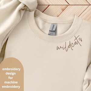 Op de afbeelding: Een beige sweatshirt met het woord "wildcats" geborduurd in bruin handschrift op de voorkant.