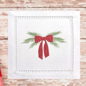 Op de afbeelding: Witte linnen servet met een rode strik en groene dennennaalden geborduurd erop.