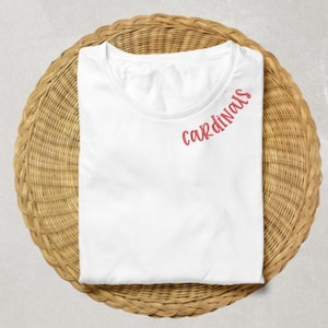 May include: White t-shirt with the word "cardinals" in red cursive lettering on the right shoulder.