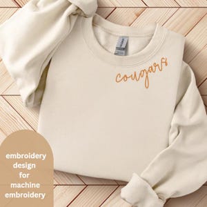 May include: A beige sweatshirt with the word "cougars" embroidered in orange on the front. This is a machine embroidery design.