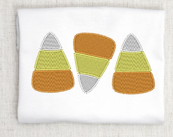 May include: Three embroidered candy corn designs in orange, yellow, and white on a white fabric background.
