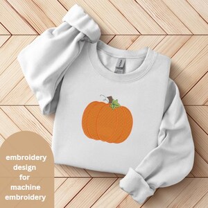 Peut inclure: Sweat-shirt blanc avec une broderie de citrouille orange et de tige verte. Le motif est centr&eacute;. Le texte "embroidery design for machine embroidery" est dans le coin inf&eacute;rieur gauche.