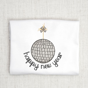 May include: A white t-shirt with a black embroidered design of a disco ball with a sparkler on top. The text "happy new year" is written around the disco ball.