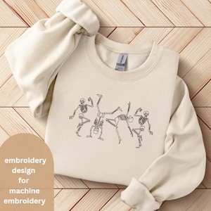 May include: Cream-colored sweatshirt featuring a black line drawing of dancing skeletons. The design includes four skeletons in various poses. The text "embroidery design for machine embroidery" is in a tan oval on the left.