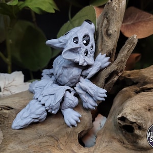 May include: A gray, furry, and detailed figurine of a wolf-like creature with multiple eyes. The figurine is perched on a piece of driftwood.