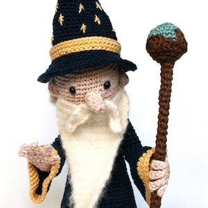 May include: A crocheted wizard doll with a blue hat, white beard, and brown staff. The hat has gold stars and a yellow band. The staff has a blue and brown orb on top.