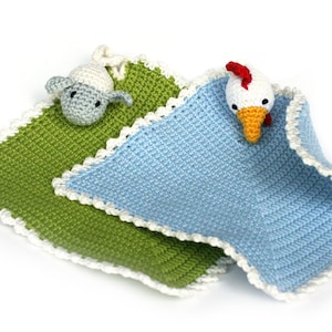以下が含まれることがあります： 動物のぬいぐるみが付いた、手編みのベビーブランケット2枚。1枚は緑色のブランケットに白い羊のぬいぐるみ、もう1枚は青色のブランケットに白い鶏のぬいぐるみが付いています。