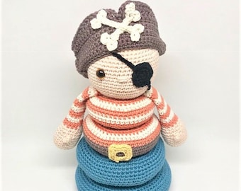 May include: Crocheted pirate doll with a brown hat featuring a white crossbones design. The doll has a black eye patch, striped shirt, and a blue base. The pirate doll is handmade and suitable for children.
