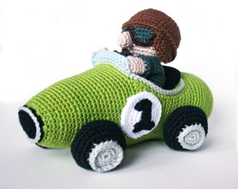 May include: A green crocheted race car with a black number "1" on the side. A crocheted person with brown hair and sunglasses is driving the car.