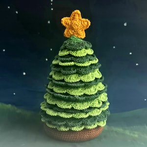 Puede incluir: Un árbol de Navidad de crochet verde con una estrella amarilla en la parte superior. El árbol está hecho de múltiples capas de tejido verde de crochet.