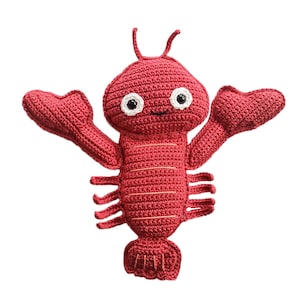 Op de afbeelding: Een rood gehaakt knuffelhoorn met witte ogen en een glimlachende mond. De kreeft heeft twee grote klauwen en een gesegmenteerde staart.