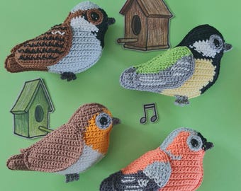May include: Four handmade crochet birds in various colors, including brown, orange, green, and gray, with black eyes. Two small birdhouses and a musical note are also present. The birds are arranged on a green background.