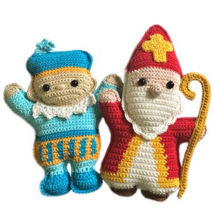 Puede incluir: Dos muñecos de ganchillo hechos a mano. Uno está vestido de azul y dorado, el otro de rojo y blanco, sosteniendo un bastón dorado. Los muñecos tienen ojos negros y están hechos con hilo suave. Probablemente sean para fines decorativos.