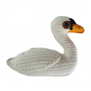 May include: A white crocheted swan with a black and brown eye and an orange beak.