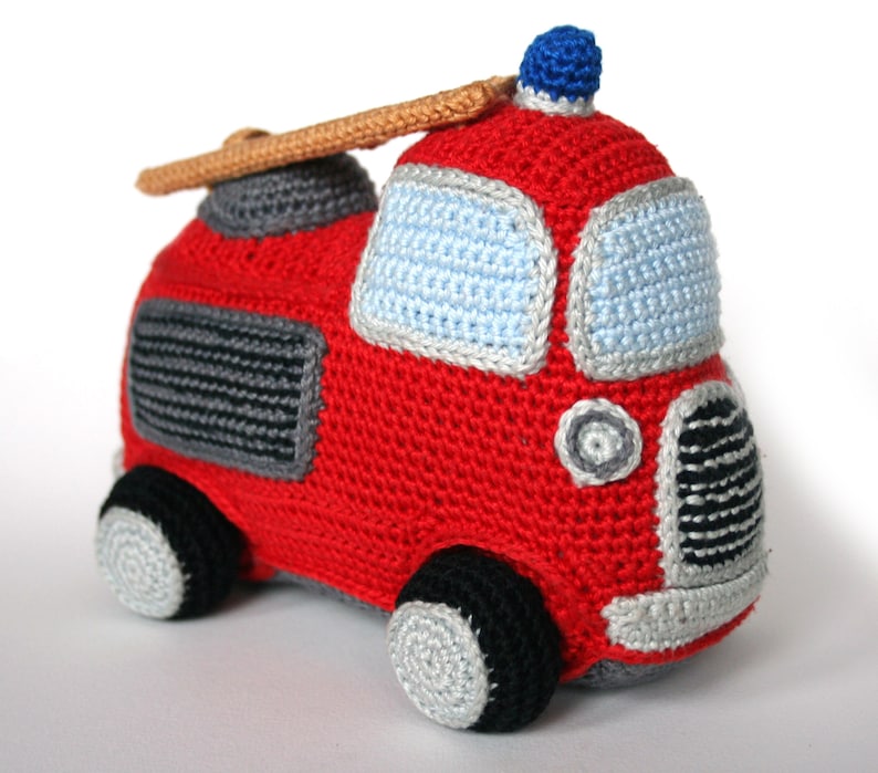 May include: A red crocheted fire truck toy with a blue light on top, a brown ladder, and black and gray details. The toy has a light blue window and black wheels with gray rims.