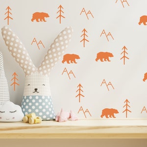 May include: A white wall with orange bear, mountain, and tree decals. Two stuffed bunny toys are in the foreground, one with a gray and white checkered pattern and the other with a blue and white polka dot pattern.