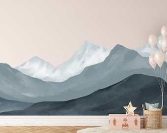 May include: A watercolor mountain range wall mural in shades of blue and white. The mural is set against a light pink background. A pink suitcase, a wicker basket, and a gold star are in the foreground.