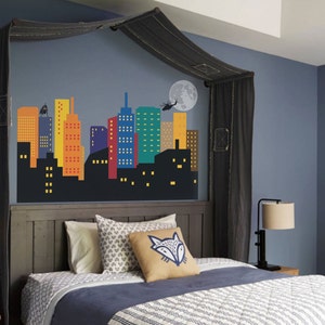 May include: A dark grey bed with a black canopy and a cityscape mural on the wall behind the headboard. The bed has a blue and white patterned duvet and a brown pillow with a fox design.