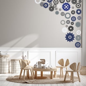 May include: A children's playroom with a light gray wall adorned with various-sized gear stickers in shades of blue, gray, and white. The room features a small wooden table, chairs, and a woven rug. Two laundry baskets and a stuffed animal are also visible.