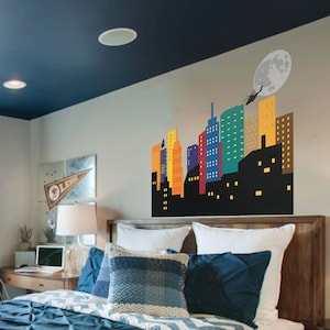 May include: A bedroom with a blue and white chevron patterned curtain, a wooden bed frame with white bedding and blue pillows, and a wall decal of a colourful cityscape with a helicopter flying over a full moon.