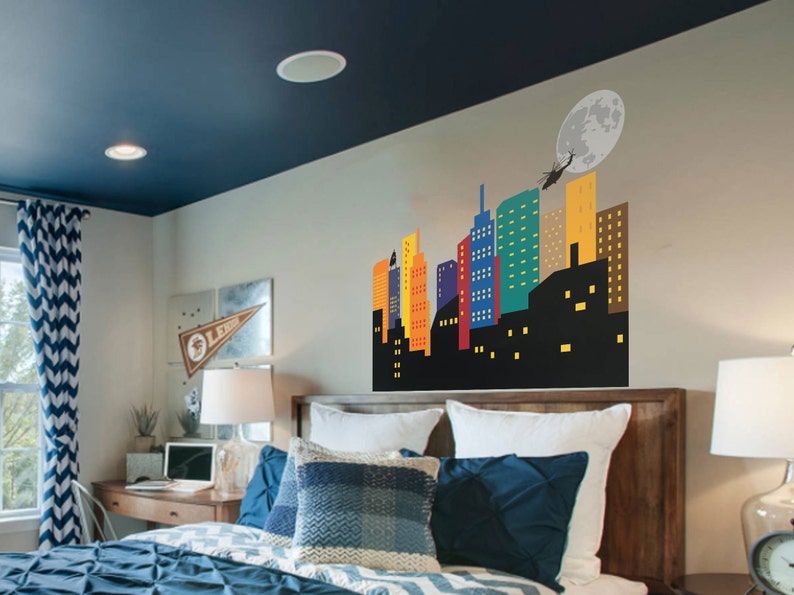 May include: A bedroom with a blue and white chevron patterned curtain, a wooden bed frame with white bedding and blue pillows, and a wall decal of a colourful cityscape with a helicopter flying over a full moon.