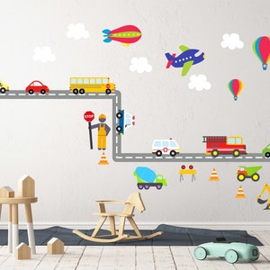 May include: A colorful wall decal set featuring a road with various vehicles, including a school bus, ambulance, fire truck, and construction vehicles. There are also clouds, hot air balloons, and an airplane. The decal set is perfect for a child's room or playroom.