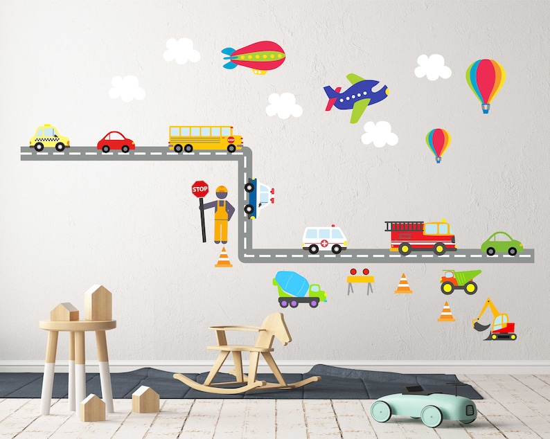 May include: A colorful wall decal set featuring a road with various vehicles, including a school bus, ambulance, fire truck, and construction vehicles. There are also clouds, hot air balloons, and an airplane. The decal set is perfect for a child's room or playroom.