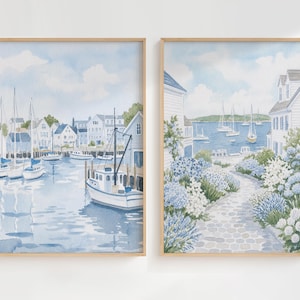 May include: Two vertical watercolor paintings in light wood frames. The left print shows a harbor with white boats and houses. The right print depicts a stone path lined with blue and white hydrangea flowers leading toward a coastal water view.